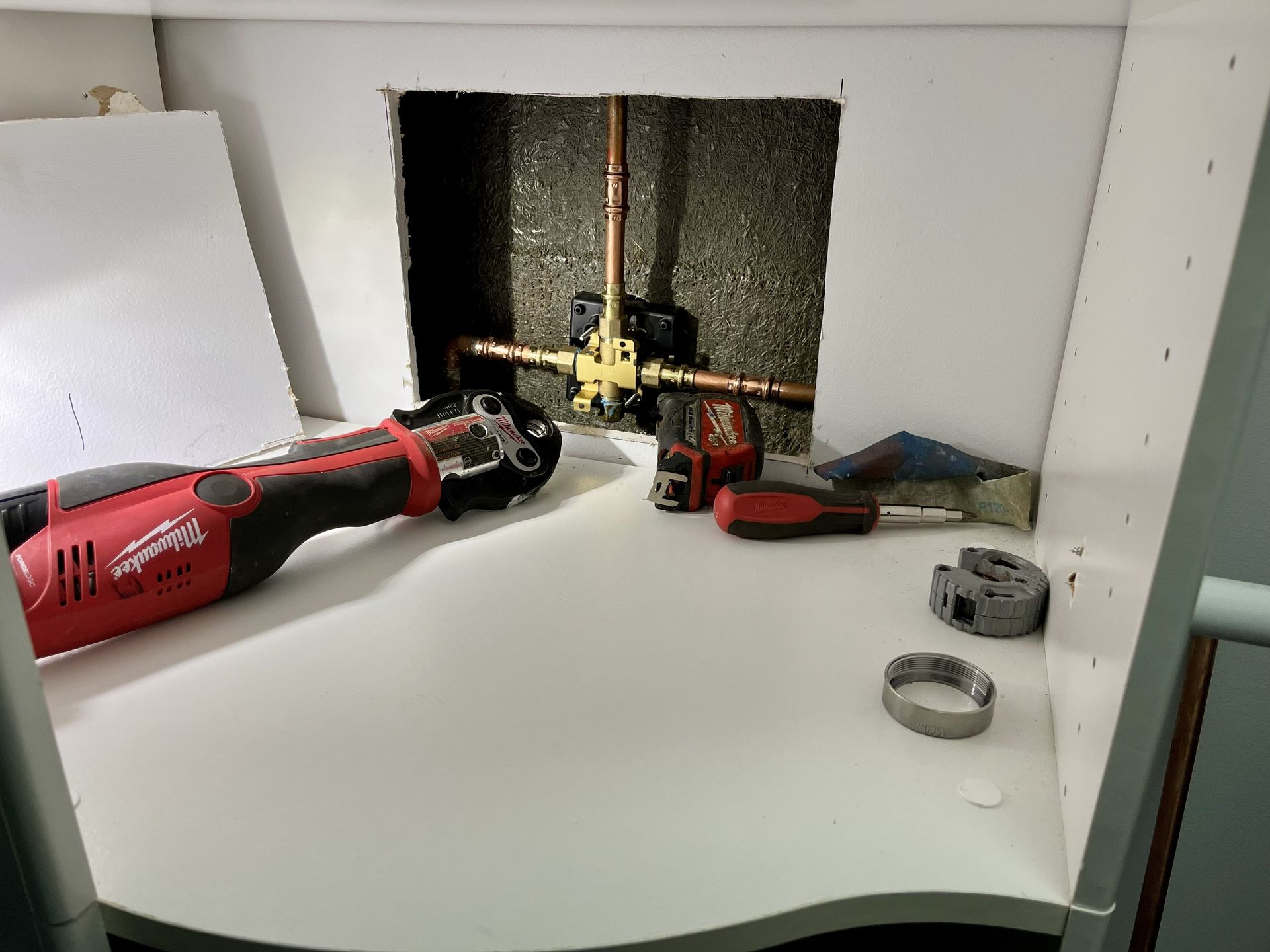 A plumbing repair in a cabinet. Copper pipes with a brass valve, a power tool, and hand tools are present.
