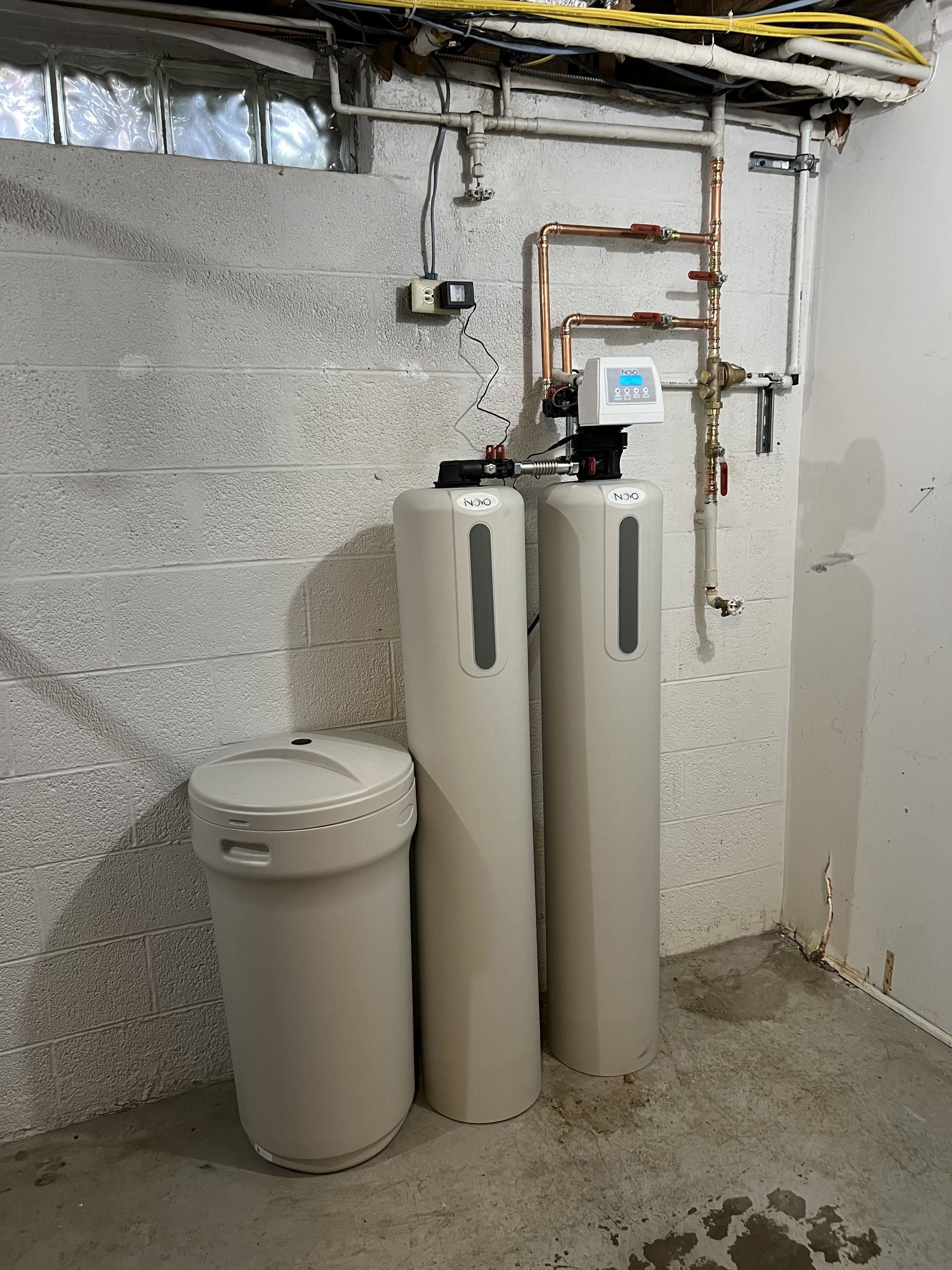 Water softener system in a basement setting with gray cinder block walls.