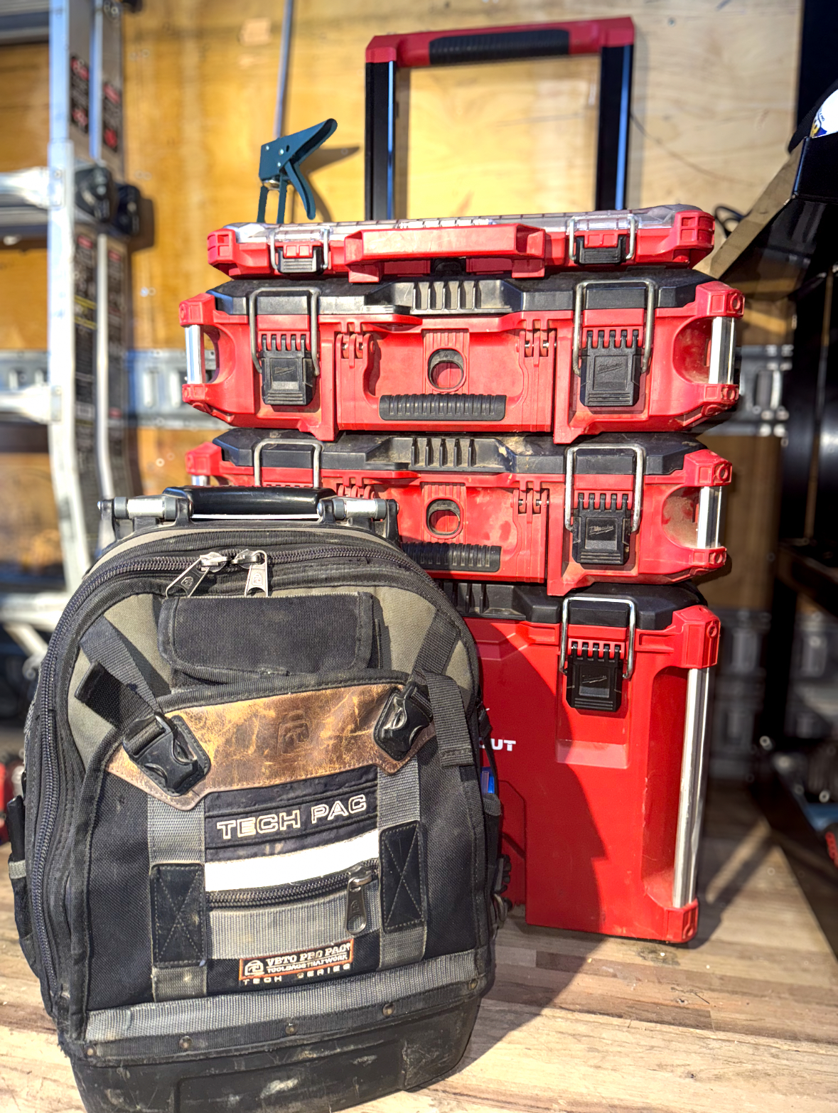 Toolboxes and a backpack, stacked. Red toolboxes, black and gray backpack in a work setting.