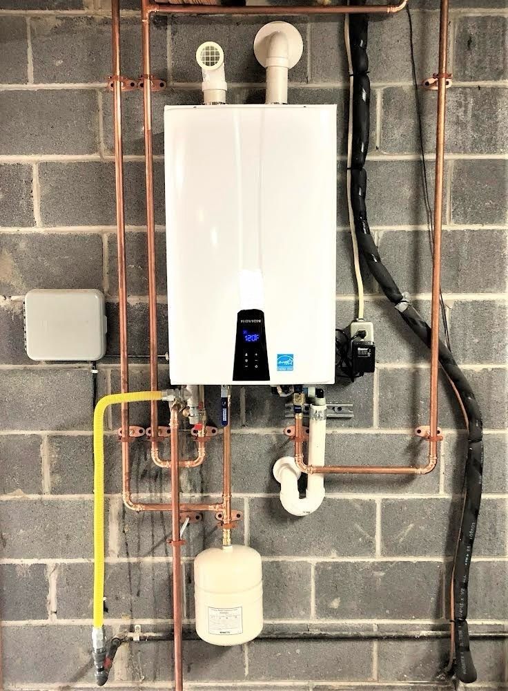 White water heater with copper pipes on a gray brick wall.