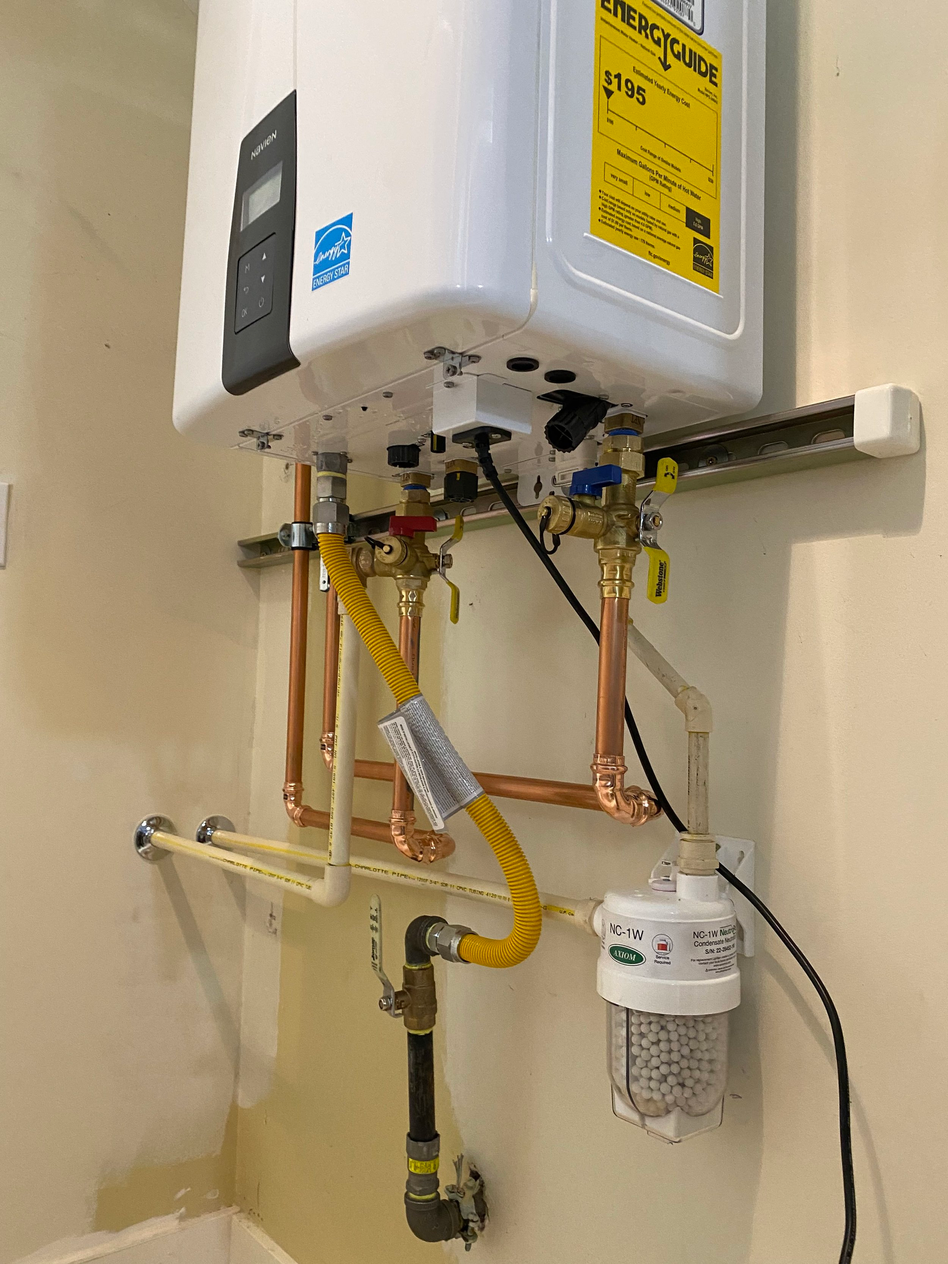 Tankless water heater installed on a wall. Copper pipes and gas line connected, with a water filter below.