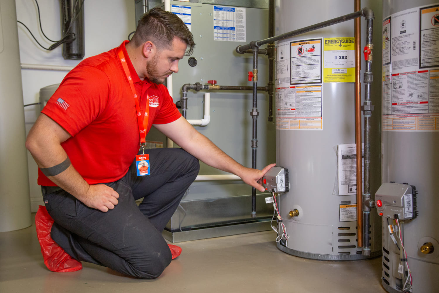 Technician in red shirt examines a water heater in a utility room.
