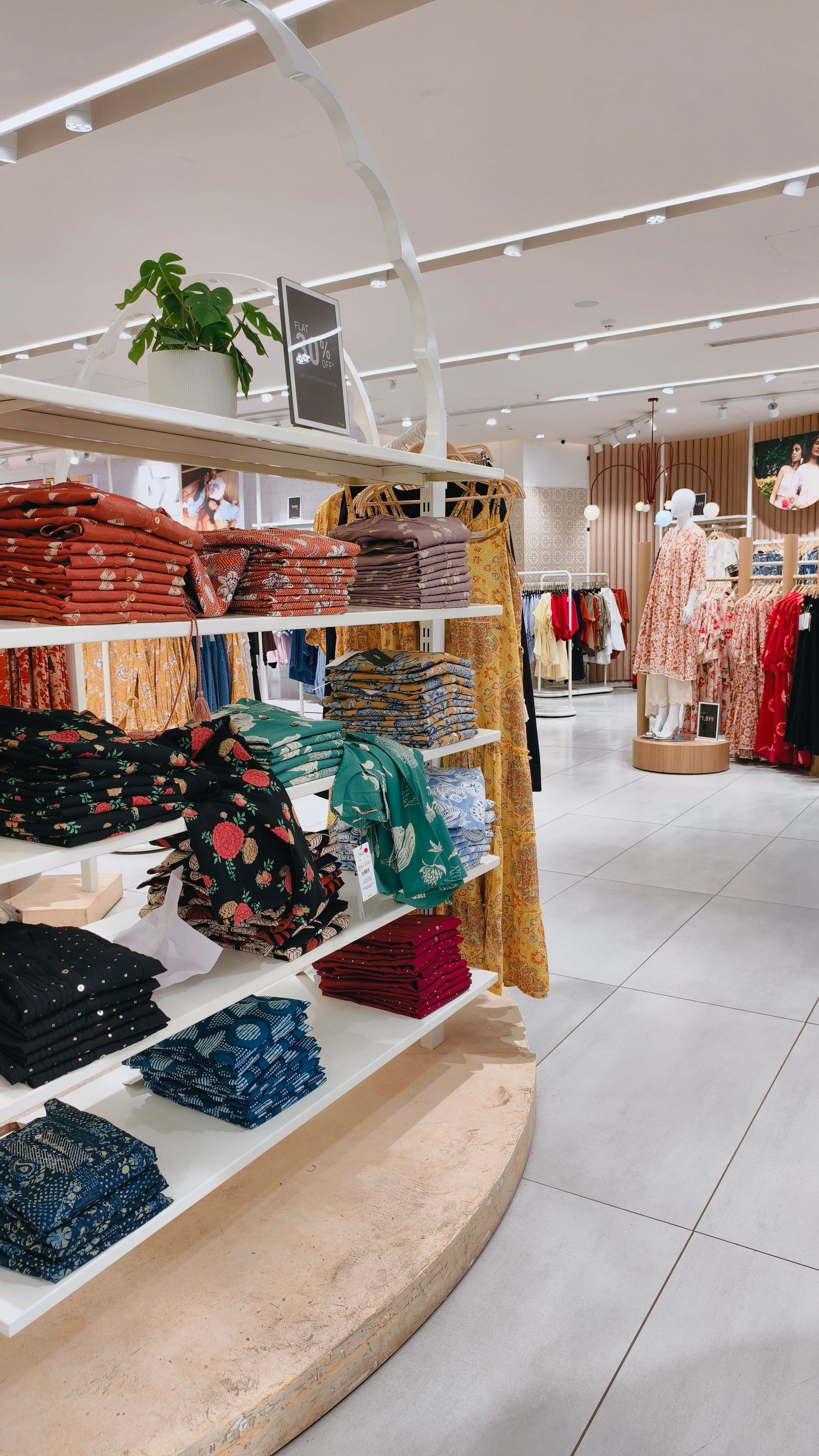 Bright clothing store interior with folded sweaters on shelves and racks of hanging dresses and garments