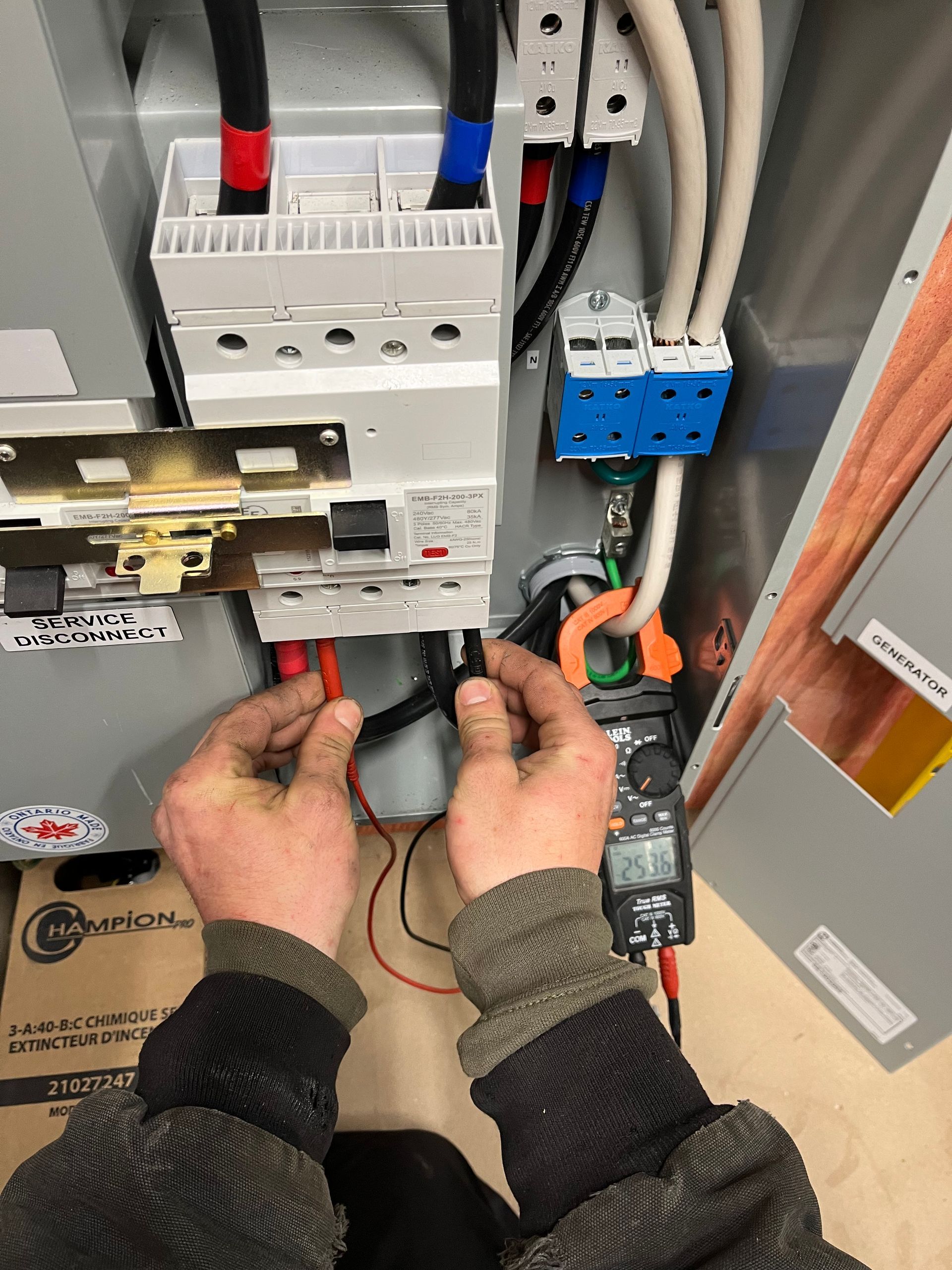 A person is working on an electrical box with a clamp and a multimeter.