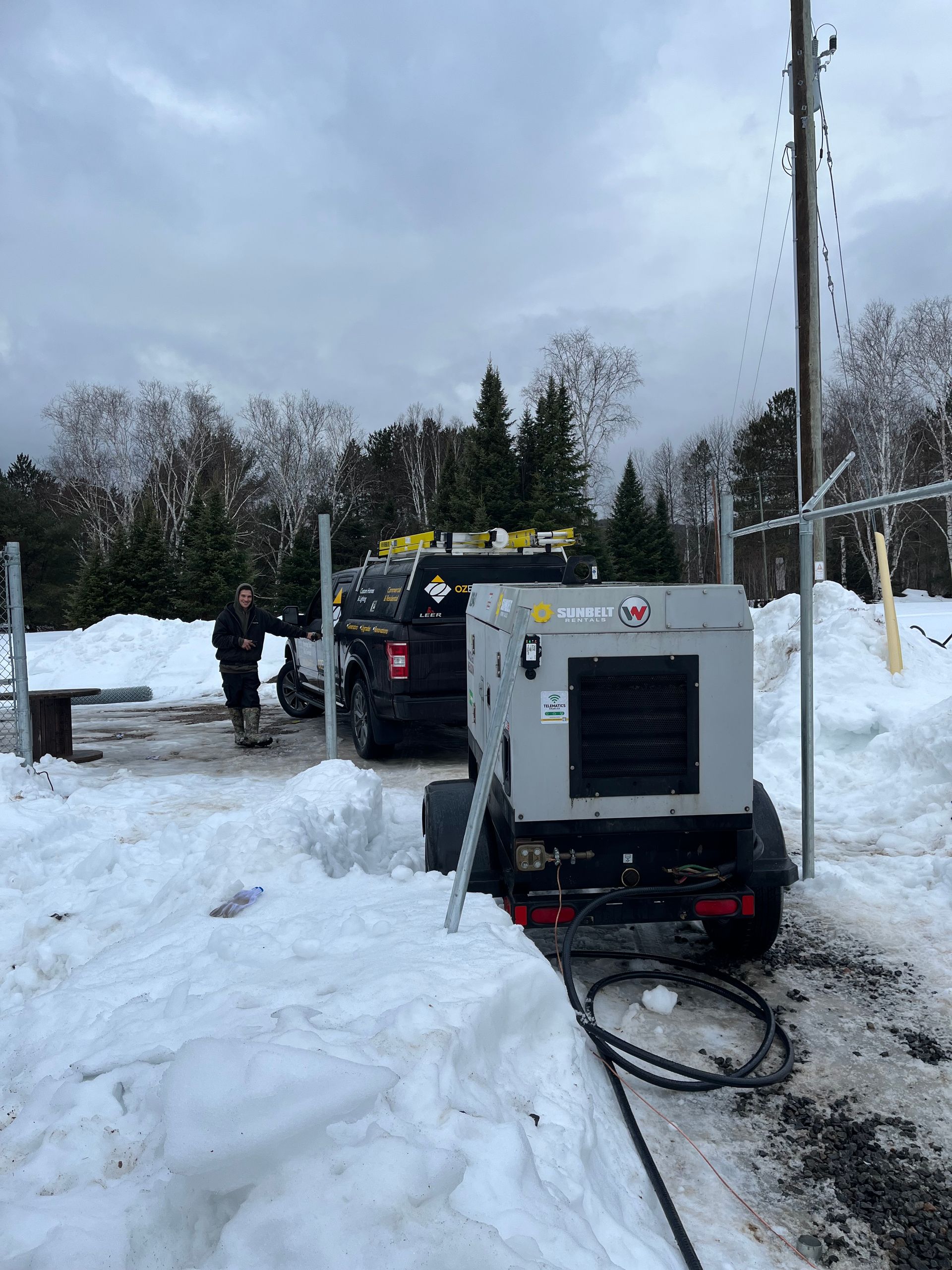 A generator is sitting in the snow next to a truck.