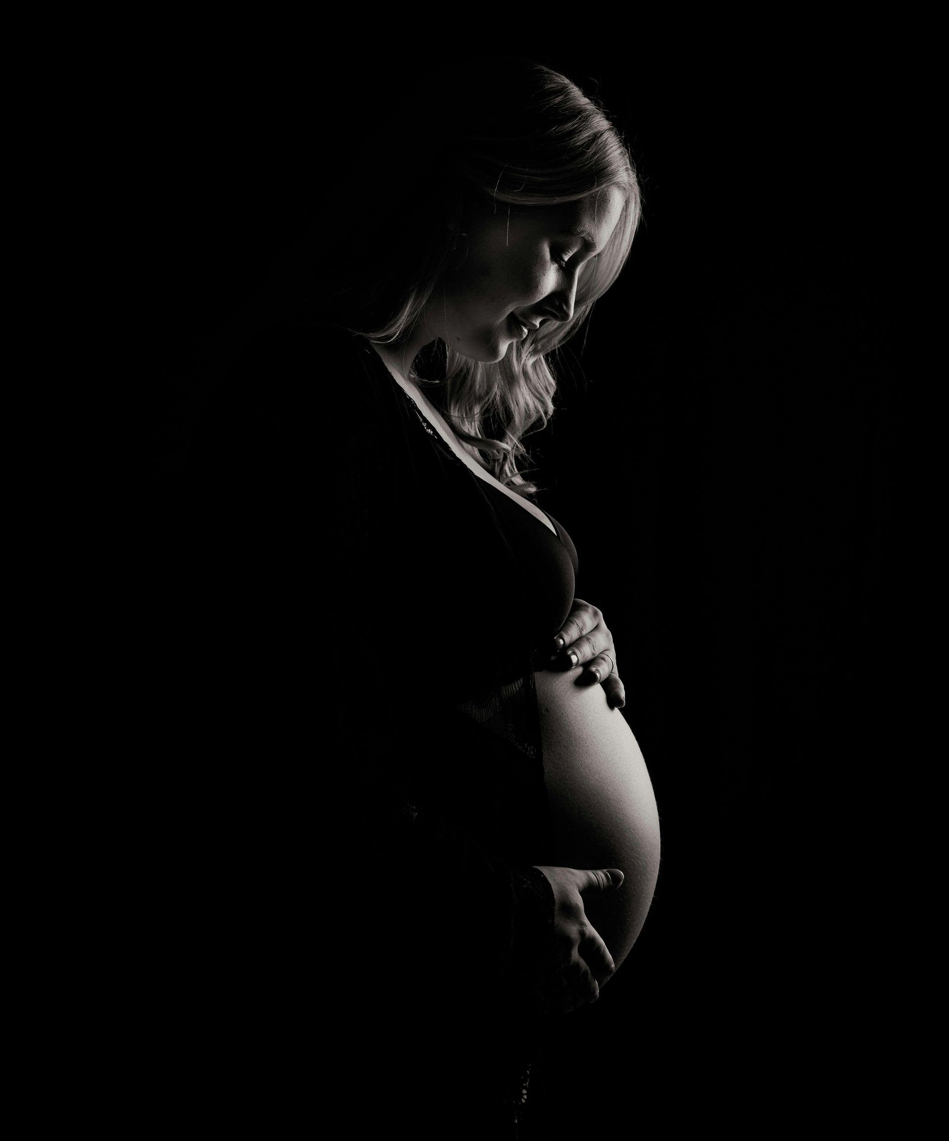 Une femme enceinte tient son ventre sur une photo en noir et blanc.