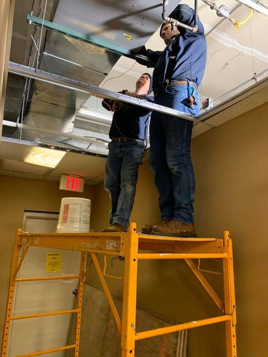 two men are working on a ceiling while standing on a scaffolding .