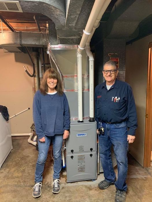 a man and a woman are standing next to a furnace in a basement .