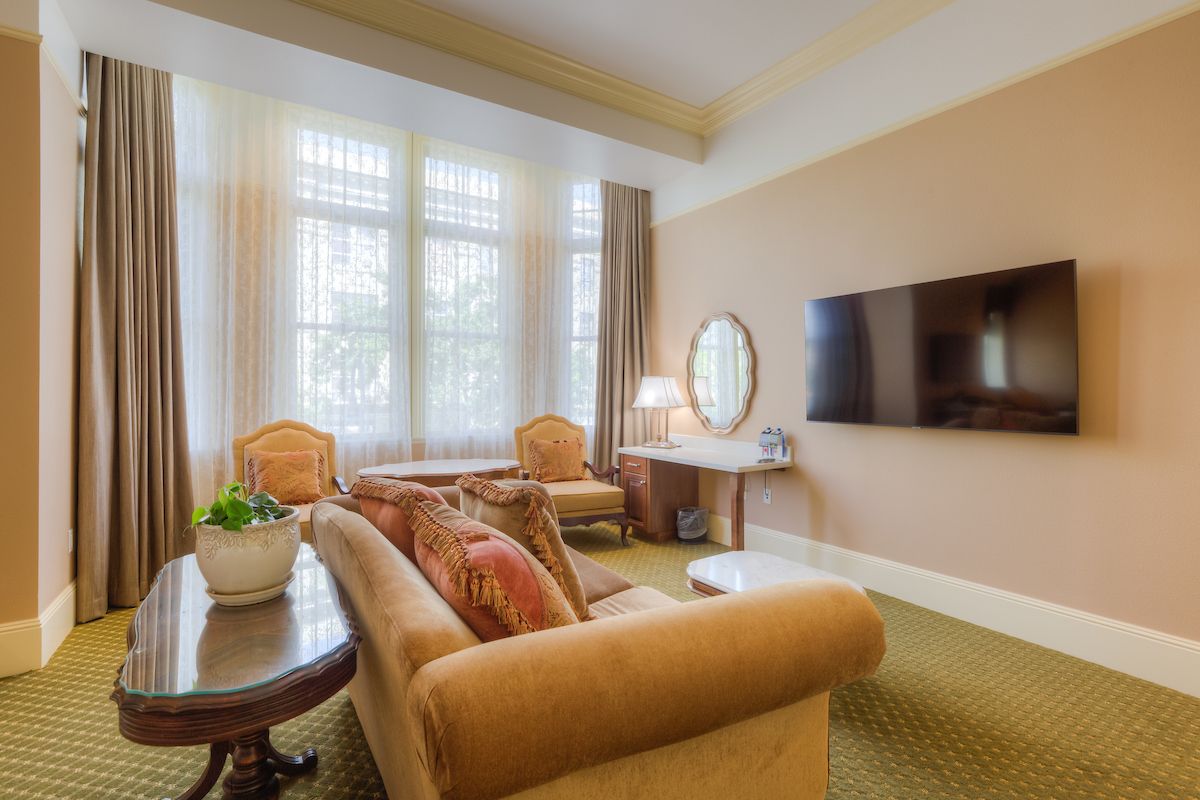Cozy living room with a beige sofa, chairs, and a round coffee table. A large window lets in natural light, and a TV.