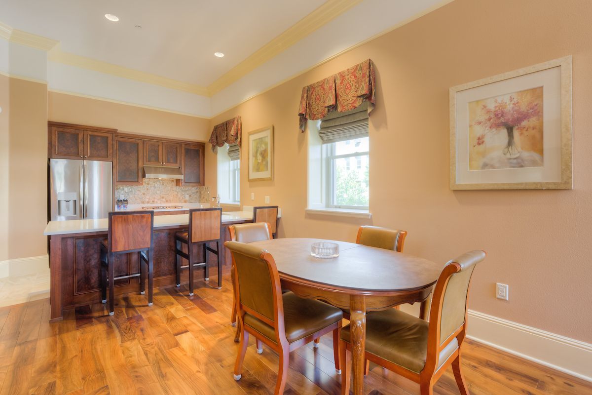 Kitchen with a wood island, counters, and barstools. A dining table and chairs sit near a window with a floral valance.