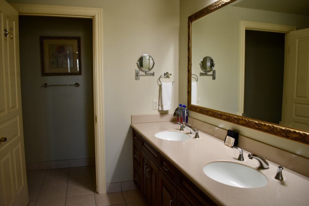 Bathroom with double sinks, large mirror, and a doorway leading to a darker room. countertop with cabinets.