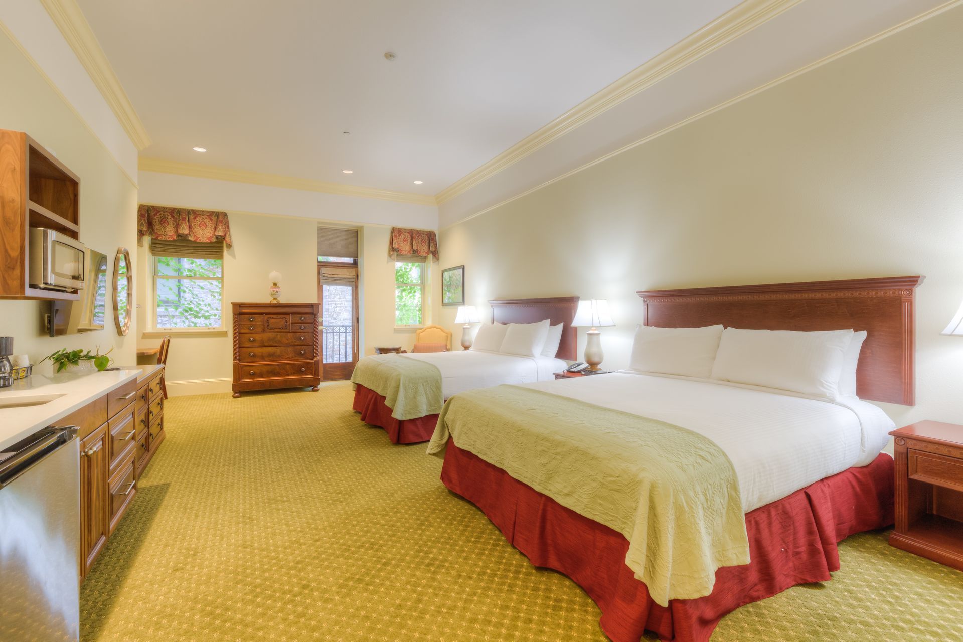 A hotel room with two double beds, a wooden dresser, and a small desk. The room has beige walls and yellow carpeting.