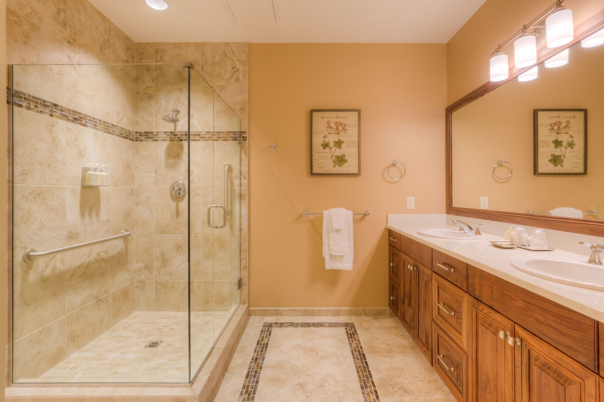Bathroom with tile shower, wooden vanity with double sinks. Decorative tile accents the shower and floor.