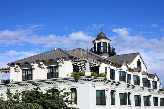 White building with dark metal roof and cupola against a blue sky.