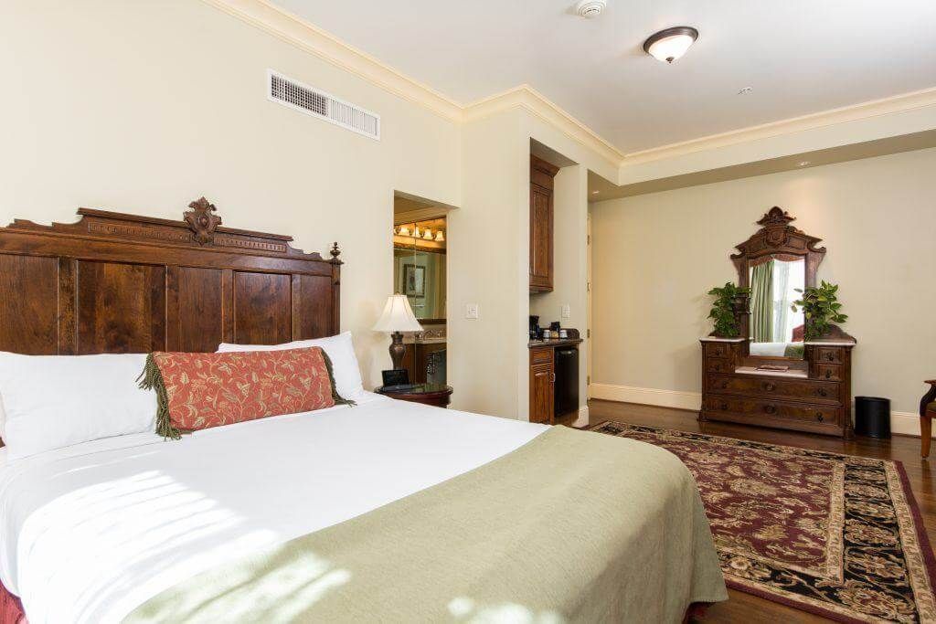 A hotel room with a large wooden bed, a decorative dresser, and a bathroom visible in the background.
