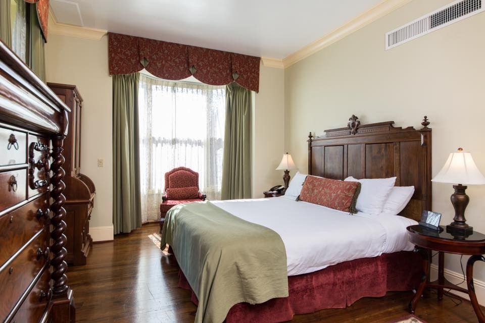 Elegant hotel bedroom with dark wood furniture, a king-sized bed, and a window with draped curtains.