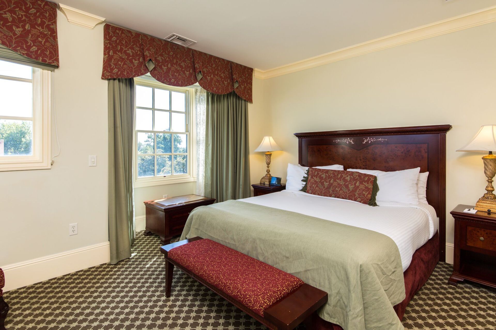 Bedroom with a queen-sized bed, two bedside tables, and a window. Features a bench and carpet, with dark wood accents.