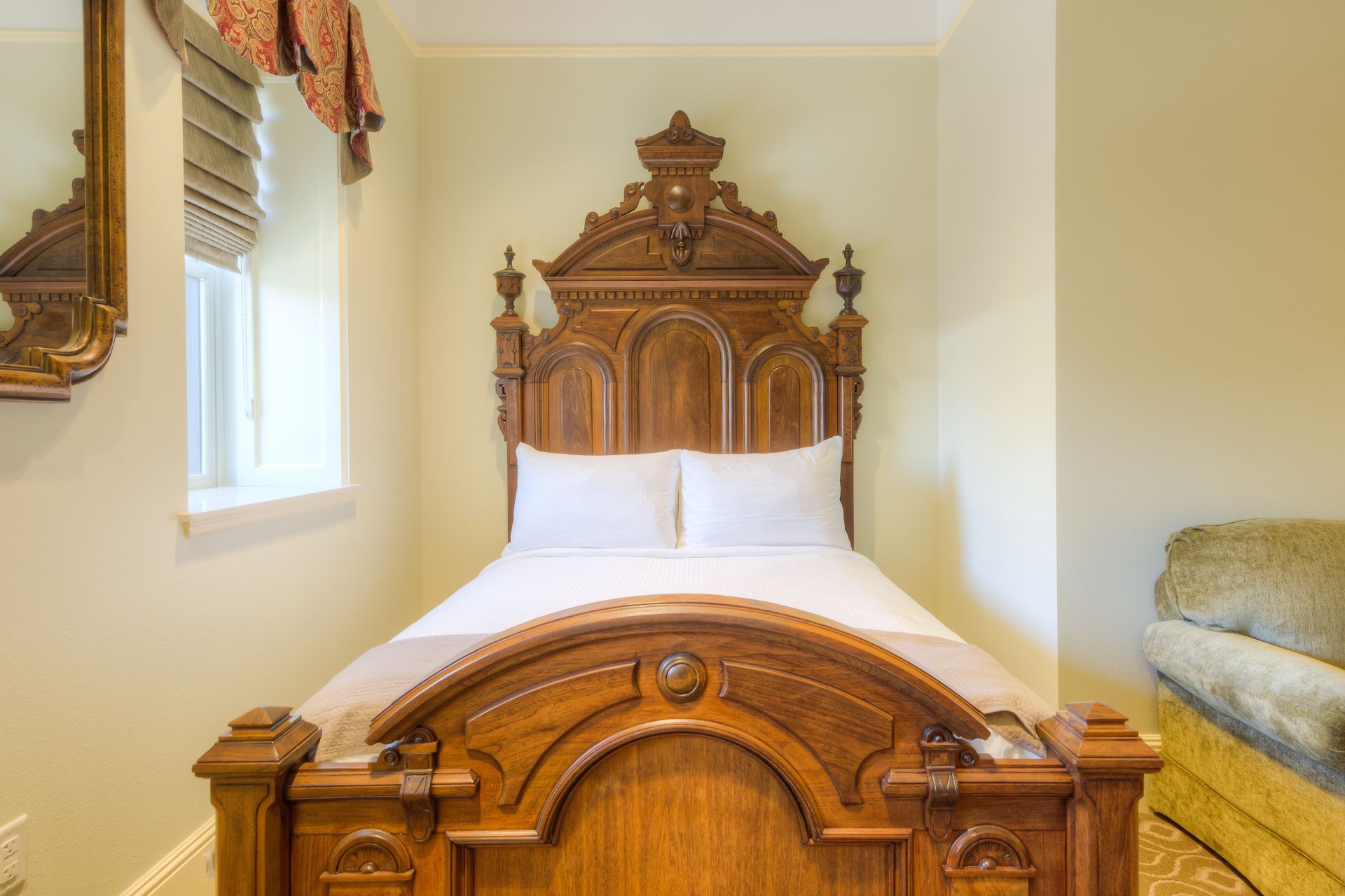A wooden bed with an ornate headboard in a small room with a window and couch.