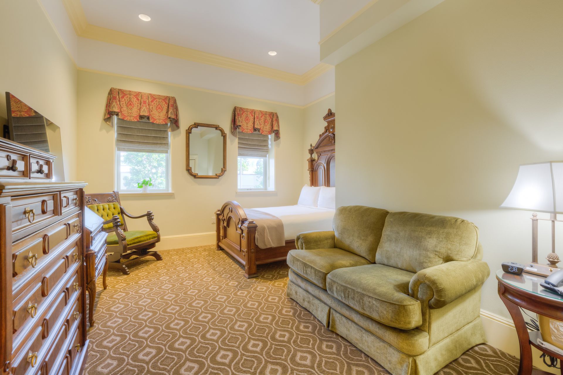 Bedroom with a bed, green sofa, ornate dresser, and two windows with matching valances. 