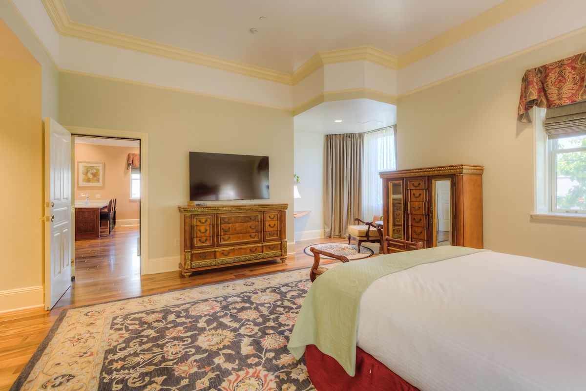 Bedroom with a large bed, ornate wooden furniture, a TV, and a doorway leading to another room.