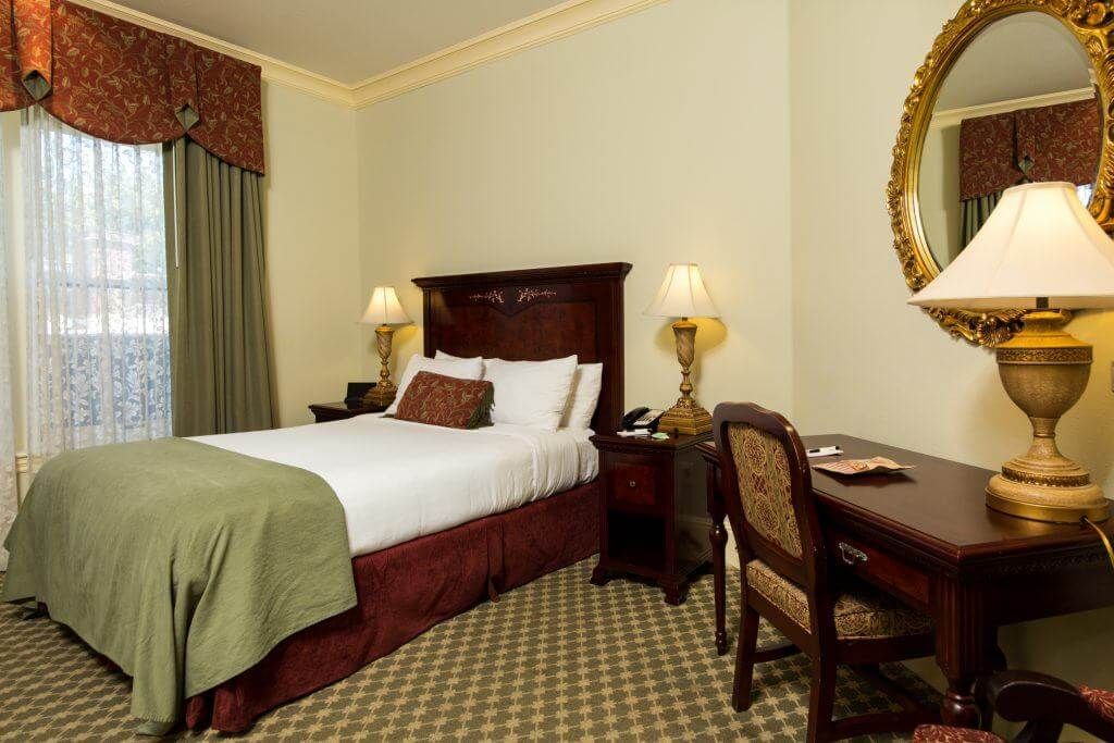 Hotel room with a single bed, desk, and a large ornate mirror. 