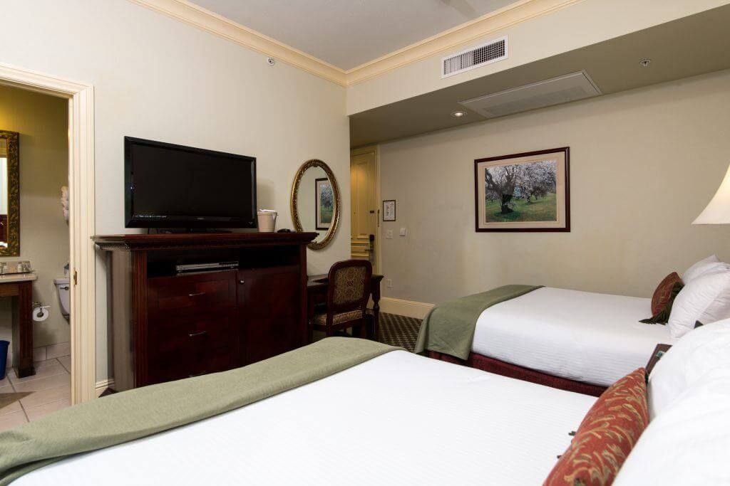 Hotel room with two double beds, a TV, and a bathroom visible to the left. 