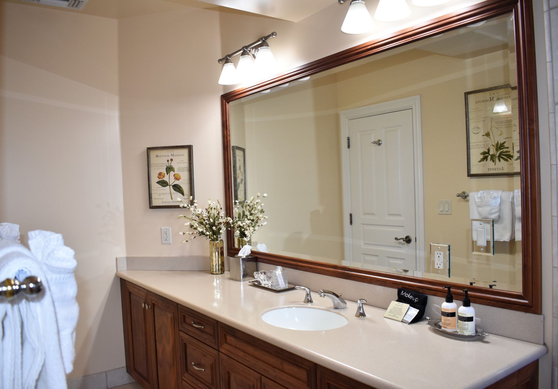 Bathroom with large mirror, wooden vanity, and light-colored countertop. Framed botanical prints adorn the wall.