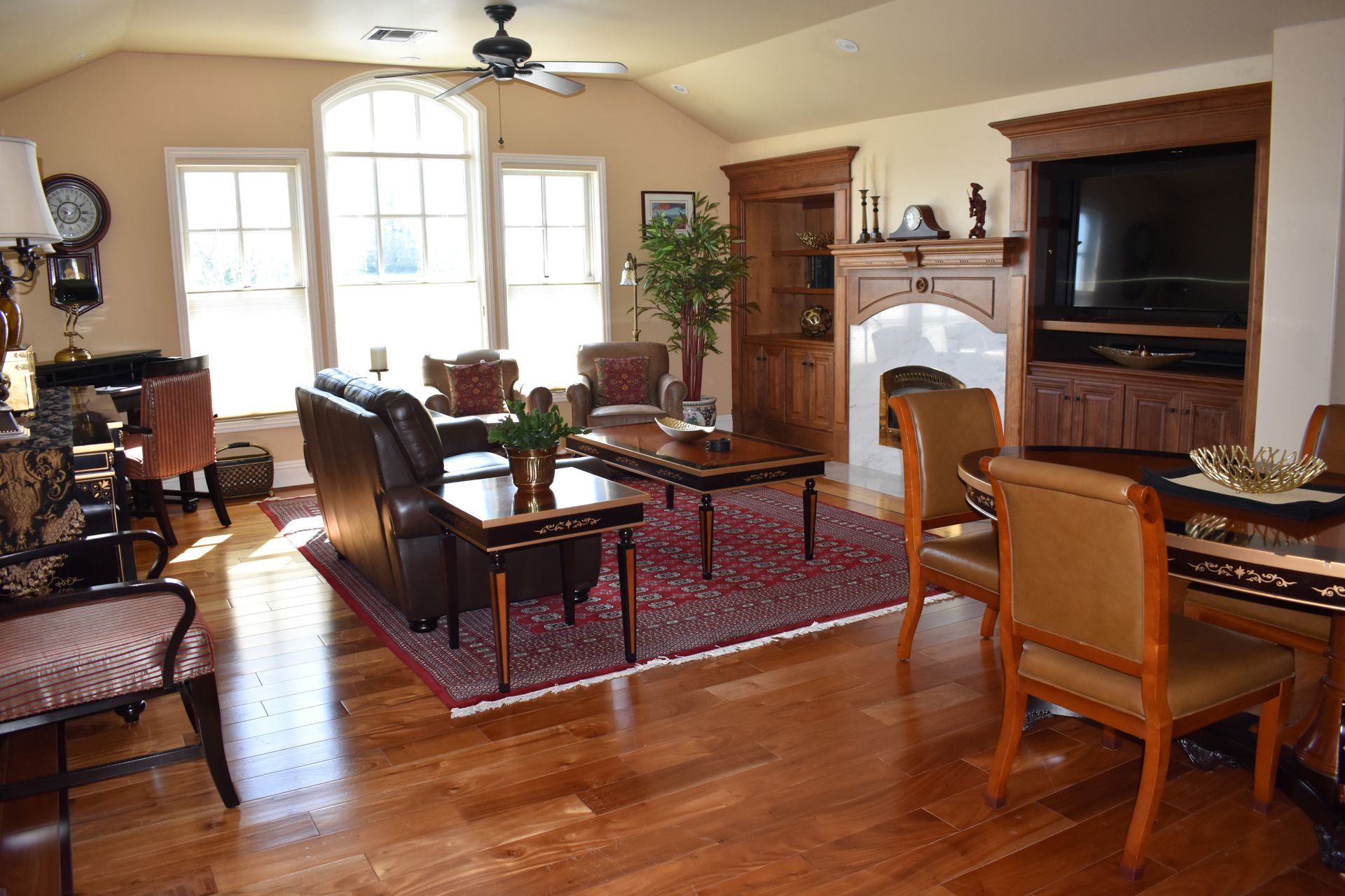 A well-lit living room with hardwood floors, a fireplace, large windows, and a mix of traditional furniture in earth tones.