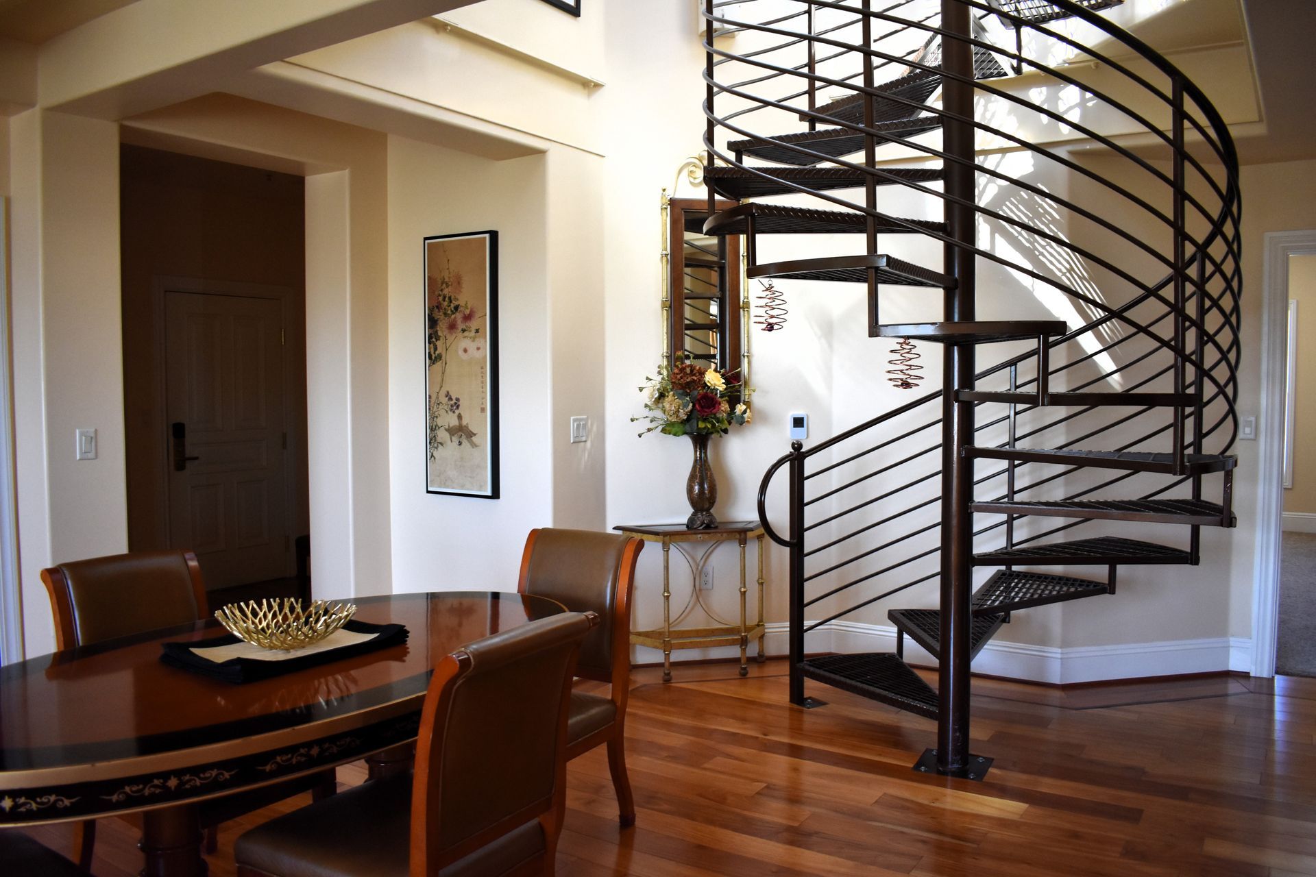 A dining room with a spiral staircase. Dark wooden table and chairs, hardwood floors, neutral walls.