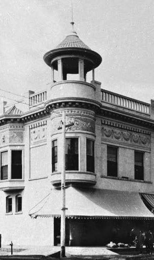 Historic corner building with a decorative turret and awning, likely from the late 1800s or early 1900s.