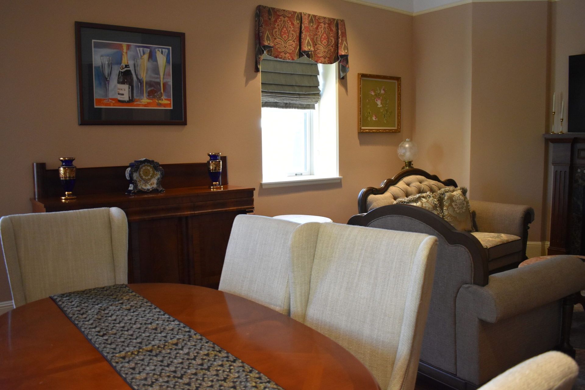 A formal dining room with a round table, chairs, a buffet, and a decorative sofa. The walls are a light brown.