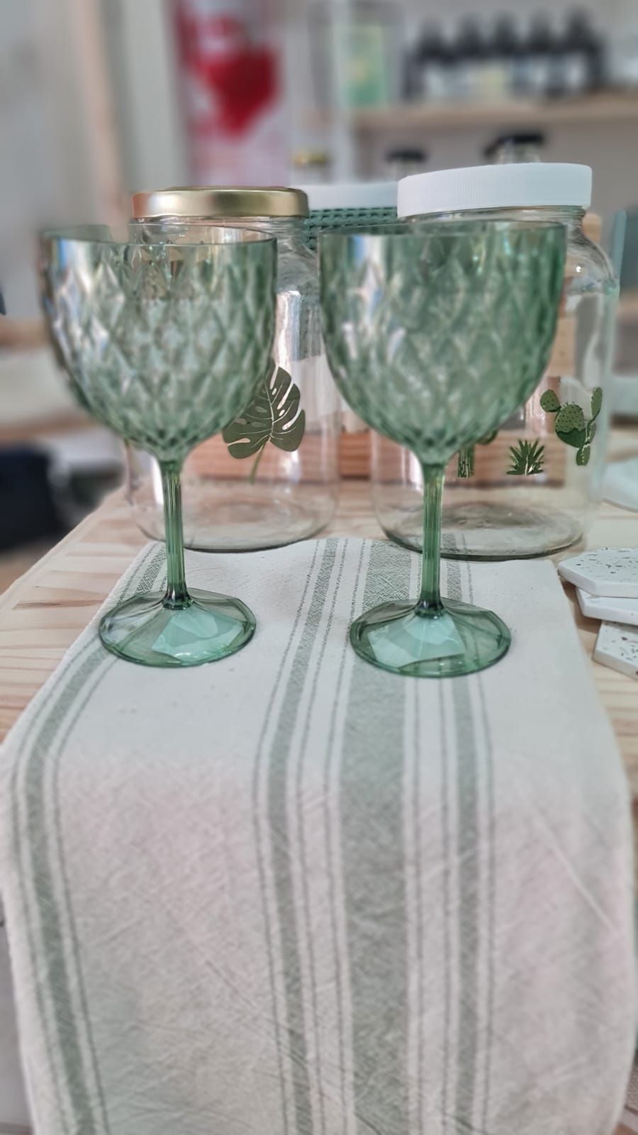 Cuatro copas con textura verde sobre una mesa de madera con pajitas, un posavasos verde claro y otra decoración.