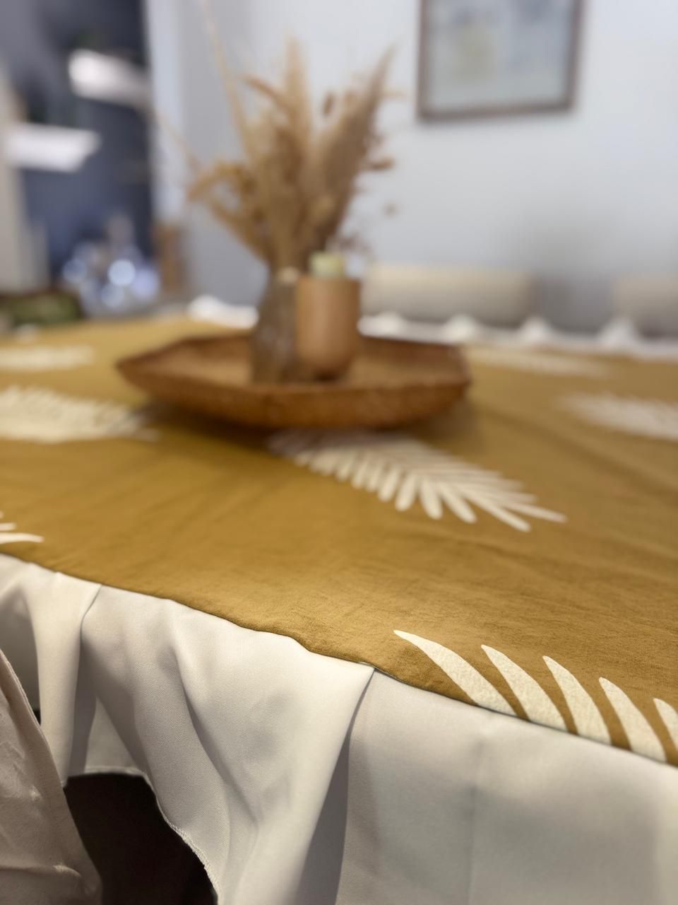 Mantel de color amarillo mostaza con dibujos de hojas blancas sobre una mesa blanca; flores secas en una bandeja.