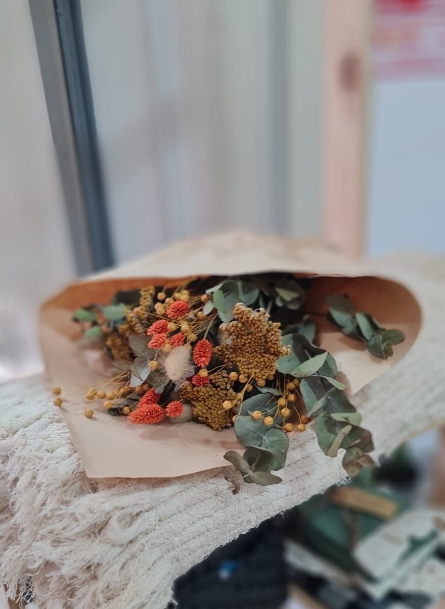 Ramo de flores secas amarillas y rosas con hojas de eucalipto verde, envuelto en papel marrón.