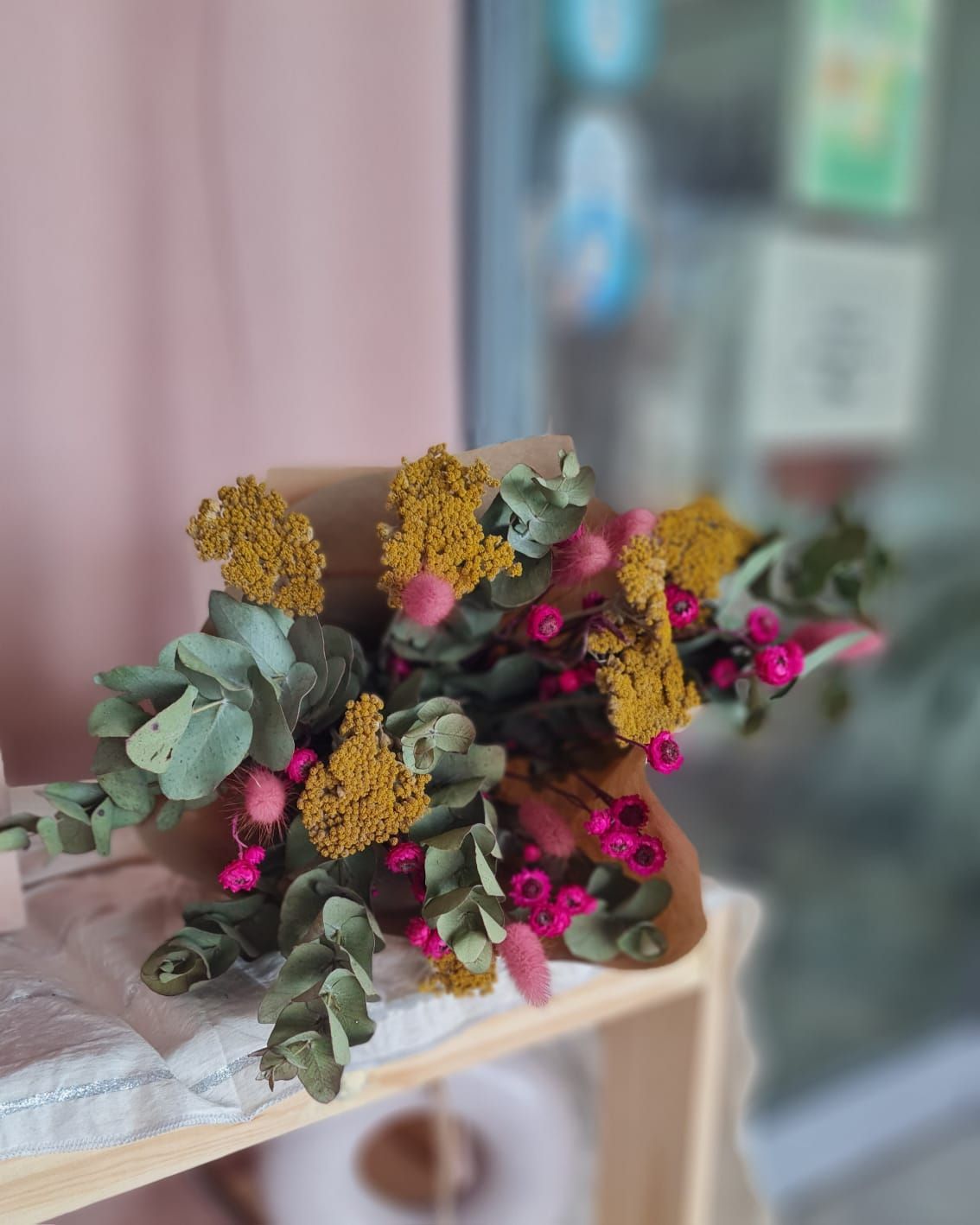 Ramo de flores secas amarillas y rosas con hojas de eucalipto verde, envuelto en papel marrón.