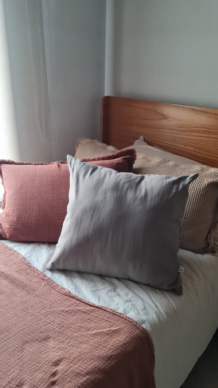 Cama con almohadas grises y rosas, manta rosa y cabecero de madera.
