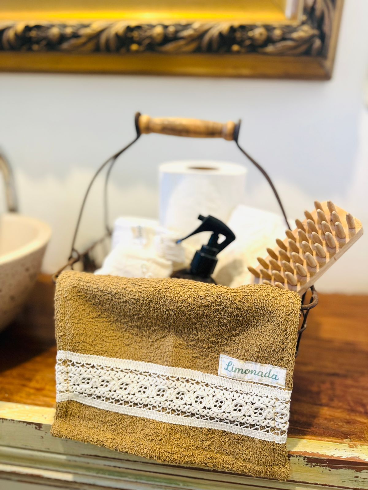 Toalla de arpillera marrón con ribete de encaje blanco sobre un toallero decorativo de cobre en un baño.