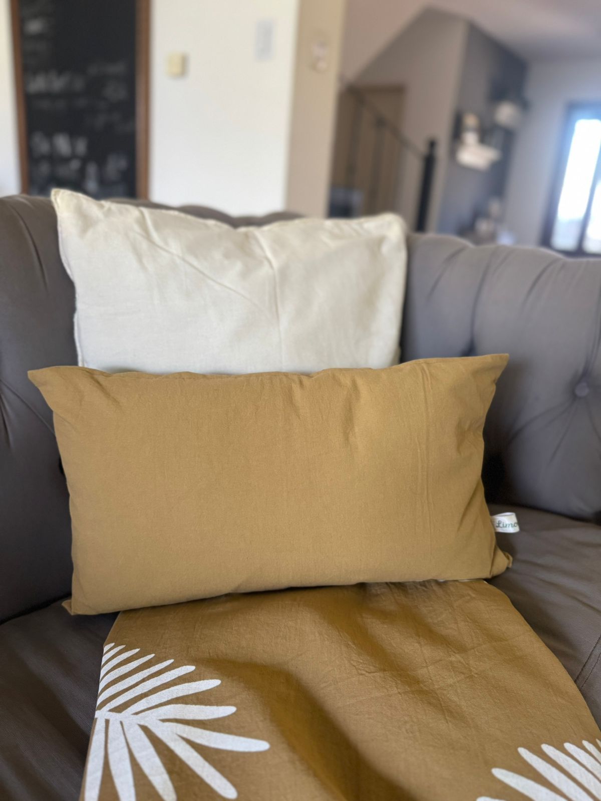 Dos almohadas, una color crema y otra mostaza, sobre un sofá capitoné gris.