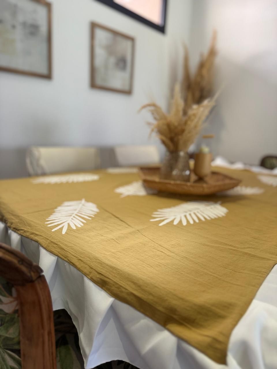 Mantel de color amarillo mostaza con dibujos de hojas blancas sobre una mesa blanca; flores secas en una bandeja.