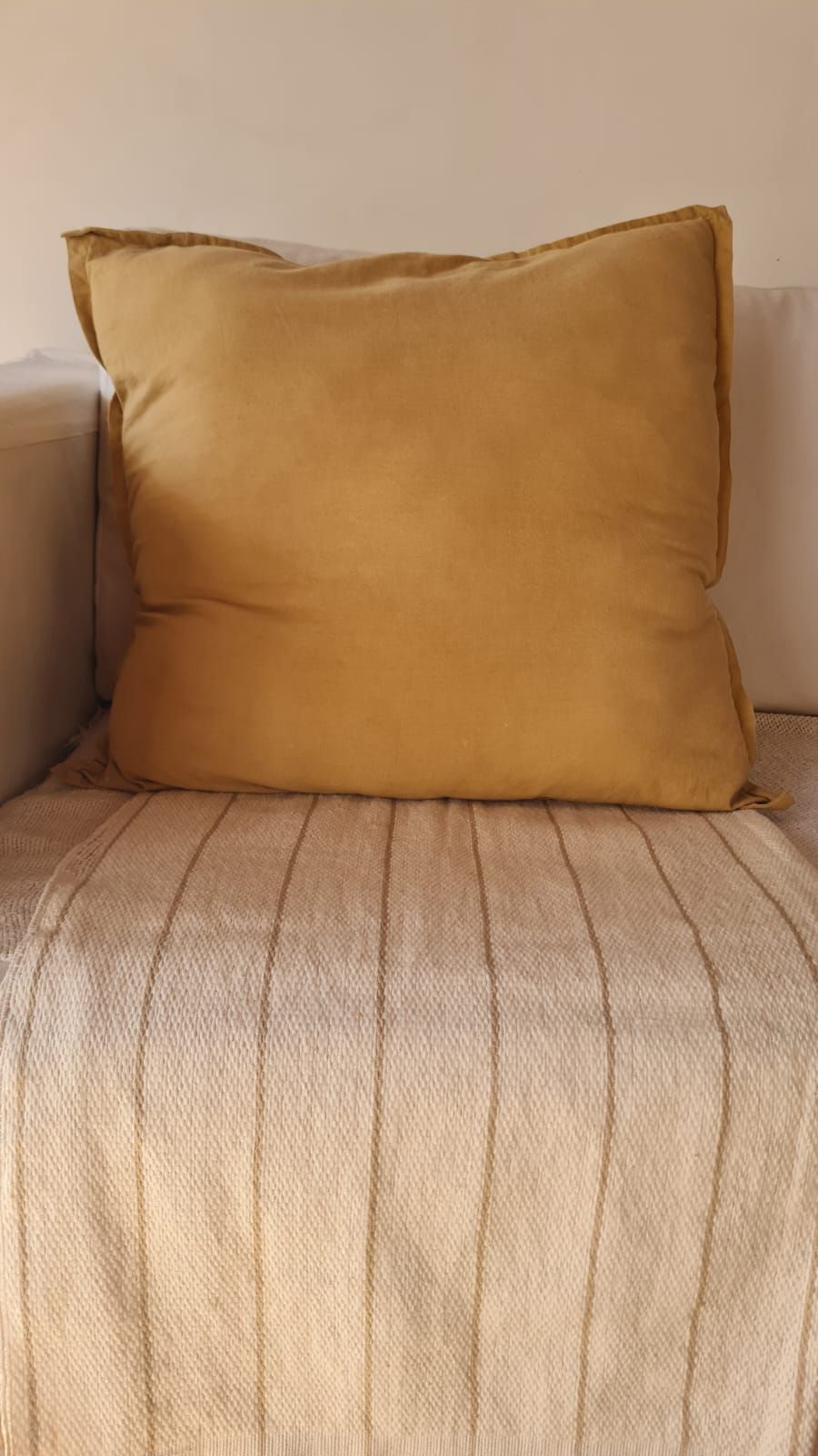 Alfombra blanca con líneas sutiles frente a una silla de madera cubierta con una manta texturizada.