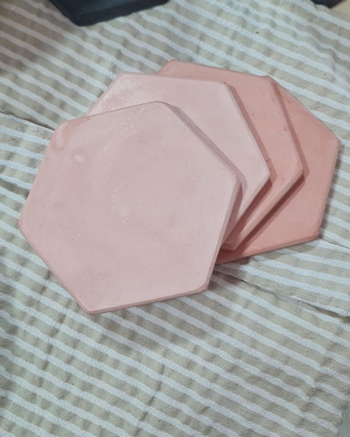 Cuatro posavasos hexagonales de color rosa apilados sobre una tela rayada.