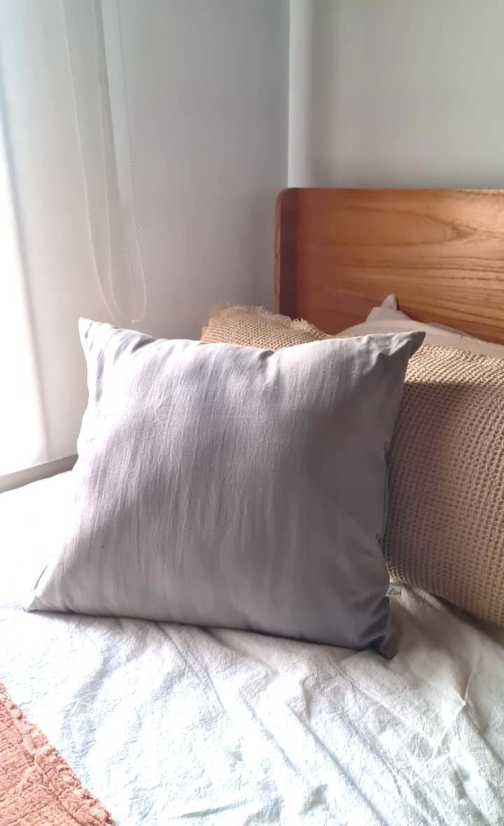 Cama con almohadas grises y rosas, manta rosa y cabecero de madera.