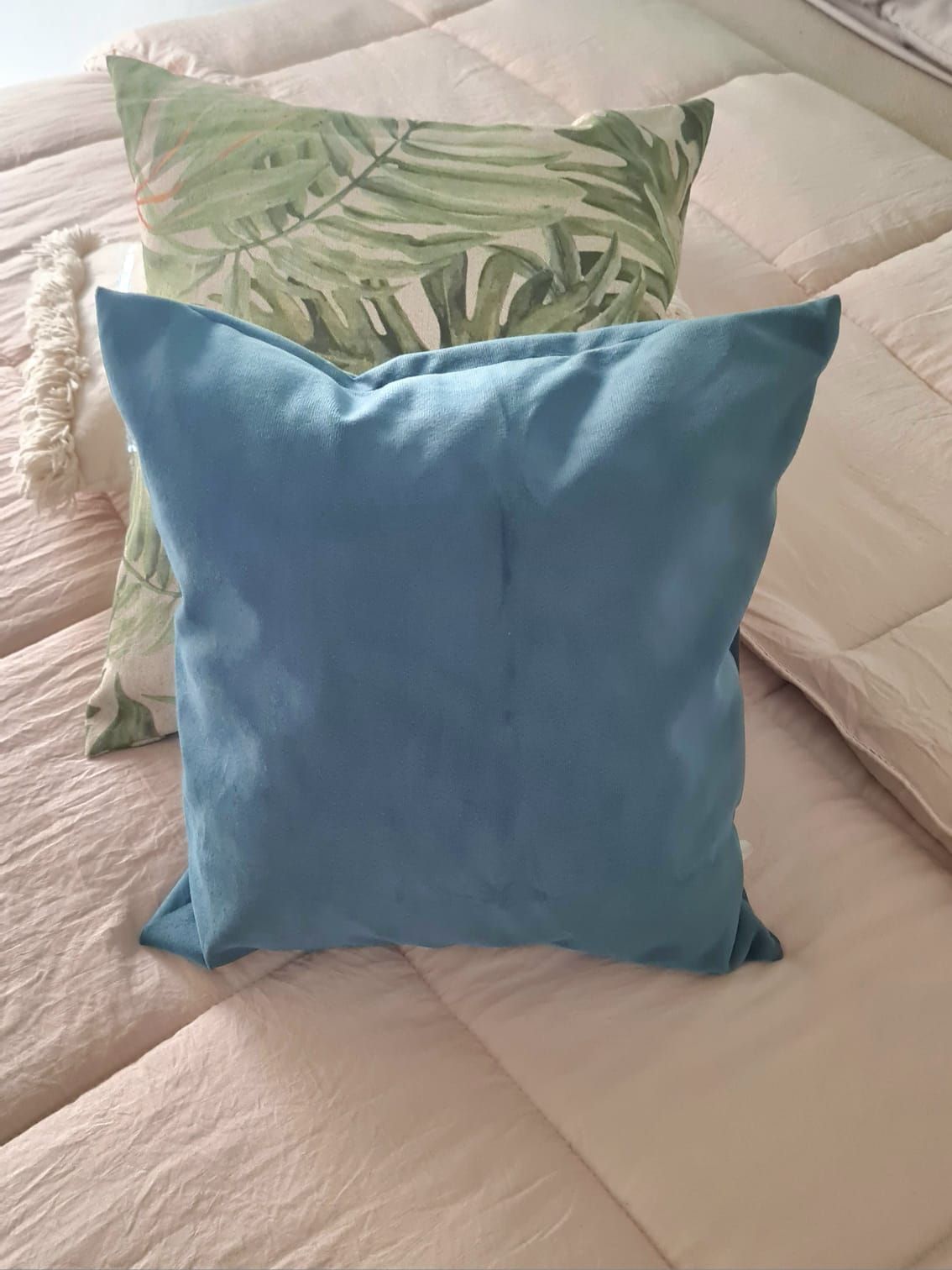 Dos almohadas cuadradas sobre una cama: una azul y otra con estampado de hojas verdes.
