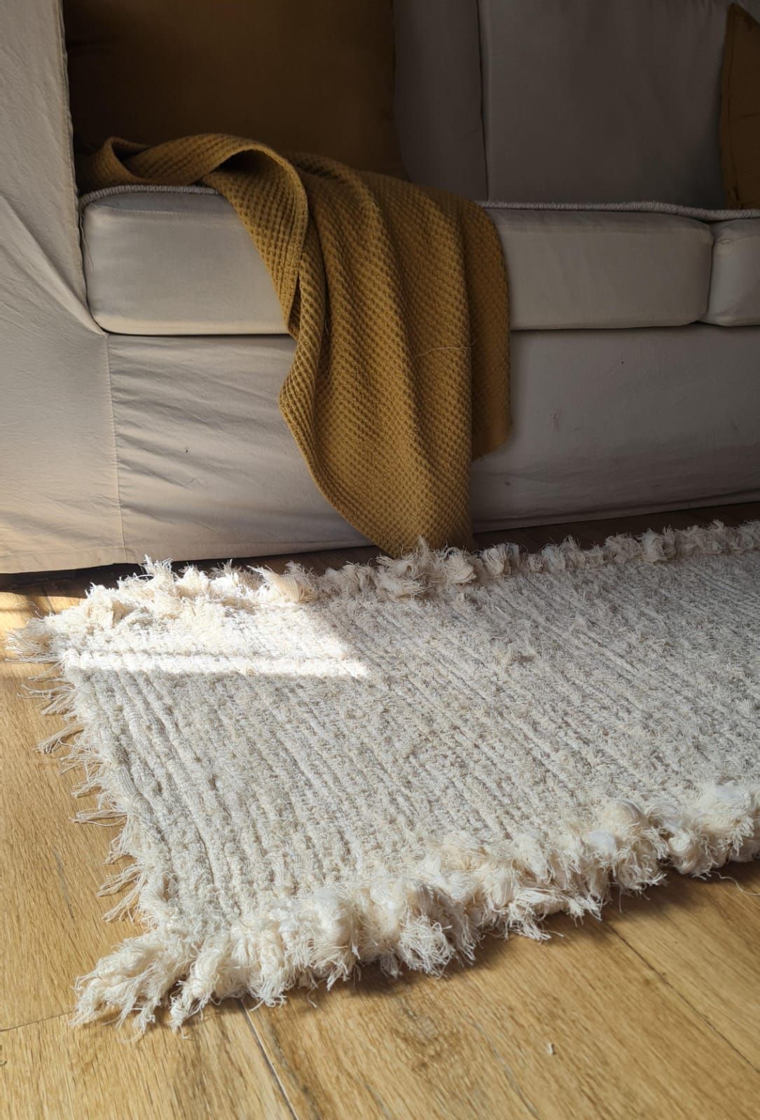 Una alfombra peluda blanca con flecos se encuentra frente a un sofá de color crema