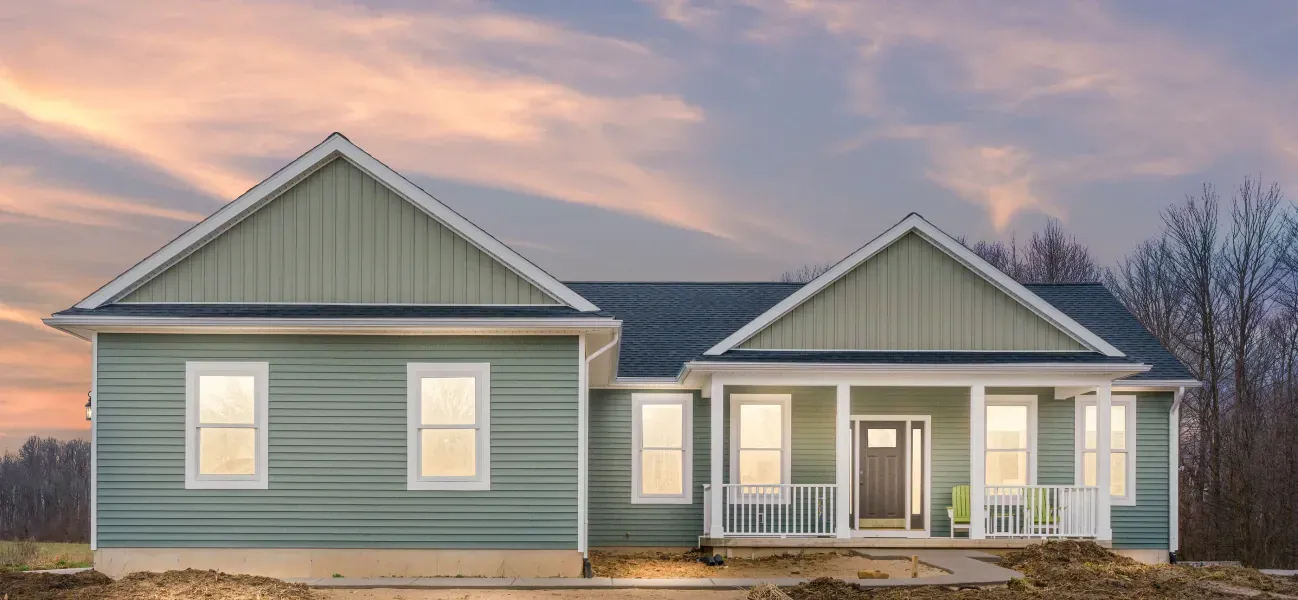 A green house with a blue roof and a porch at sunset.