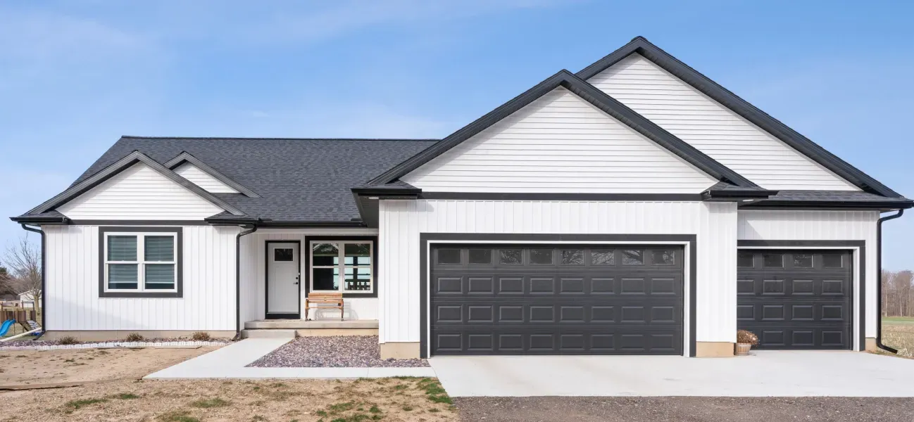 A white house with black garage doors and a black roof.