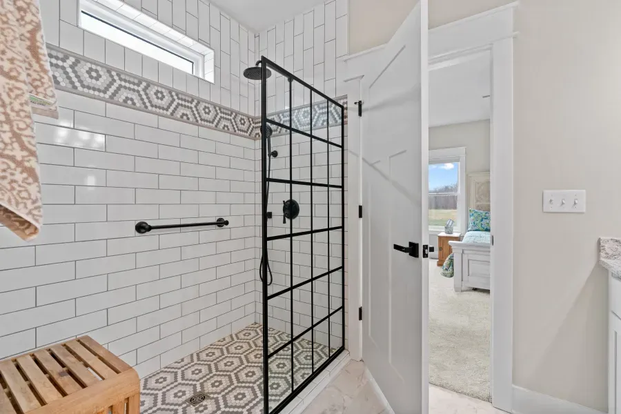 A bathroom with a walk in shower with a black glass door.