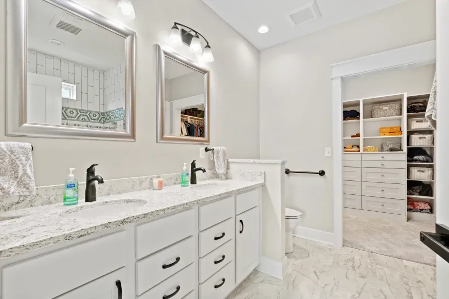 A bathroom with two sinks , two mirrors and a walk in closet.