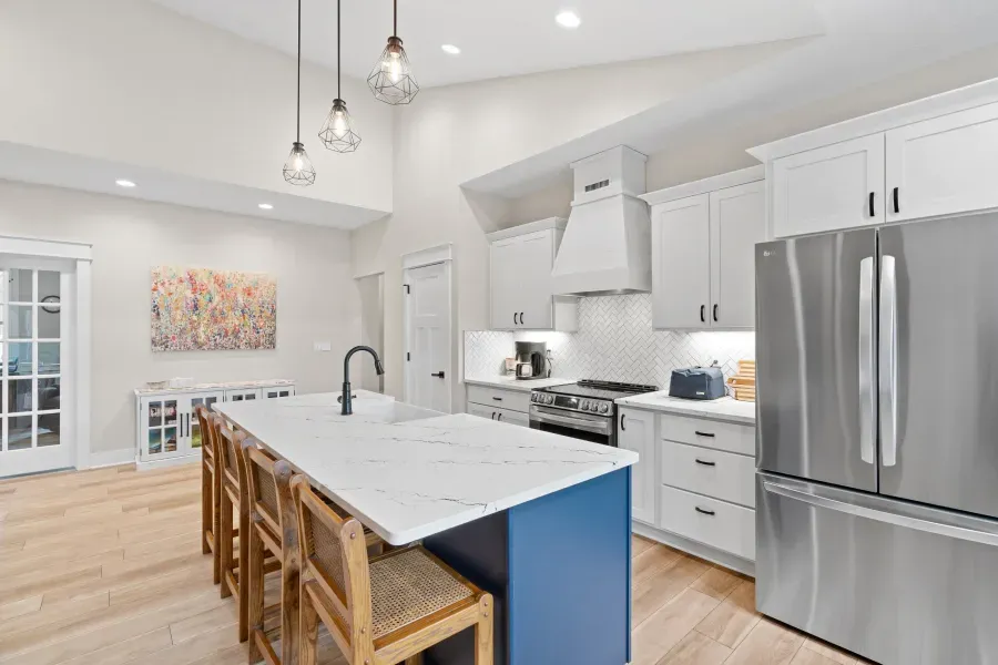 A kitchen with white cabinets , stainless steel appliances , a large island , and a refrigerator.