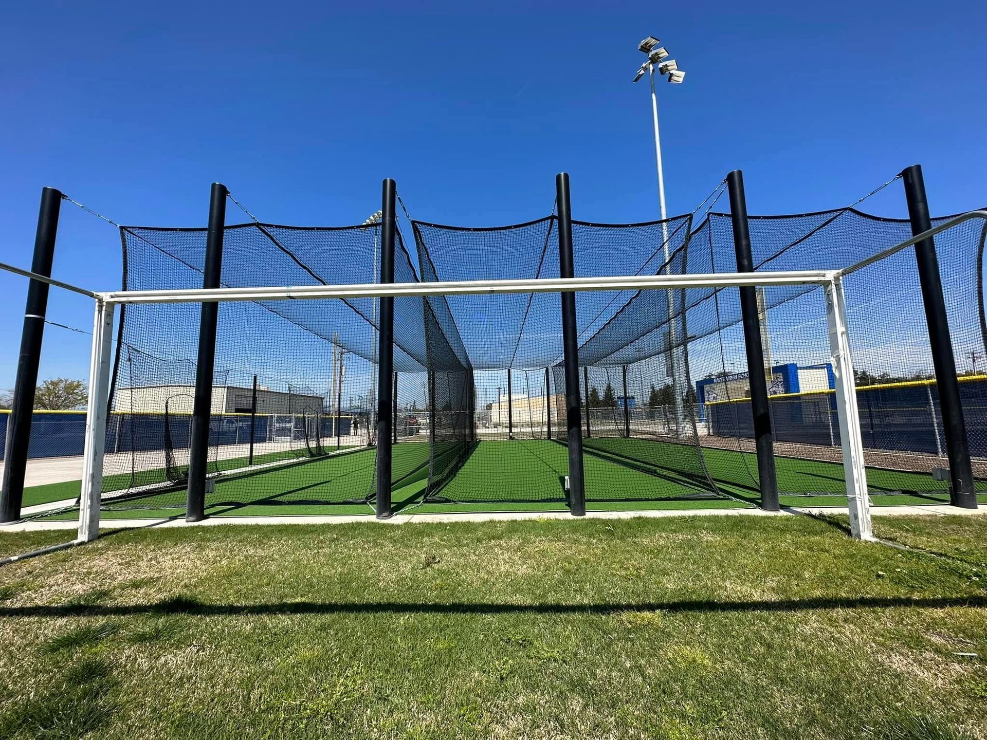 Soccer goal on a grassy field with tall black netting and a clear blue sky